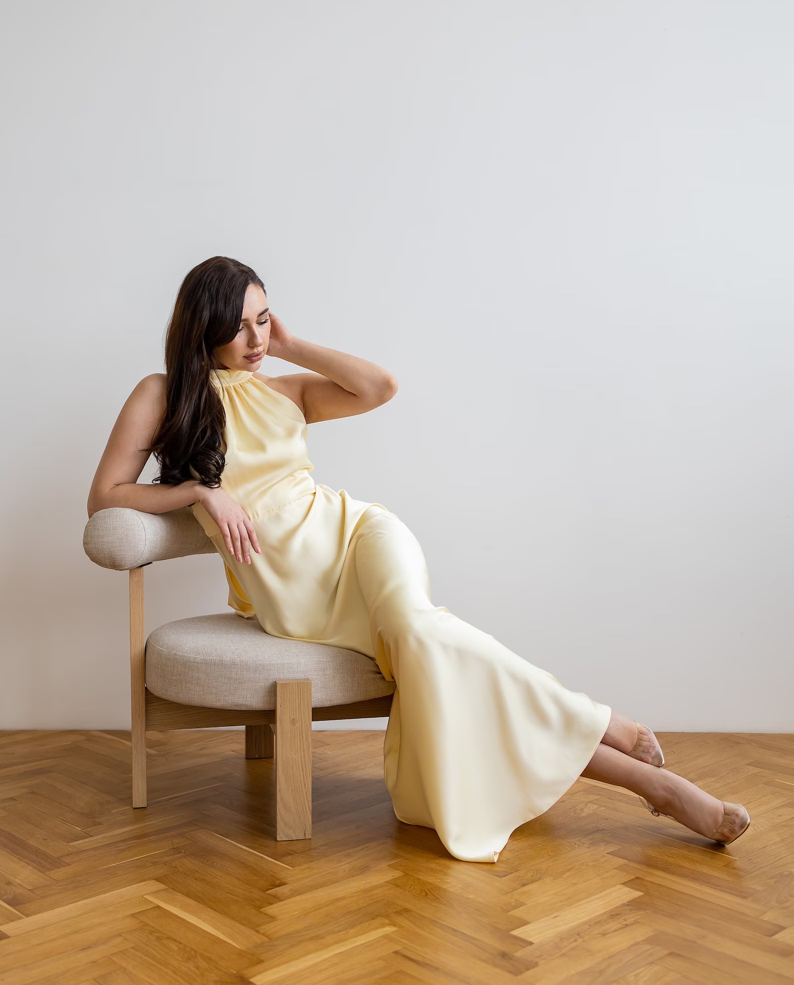 Rochie din satin galben-pal cu guler halter, purtată de o femeie așezată pe un fotoliu